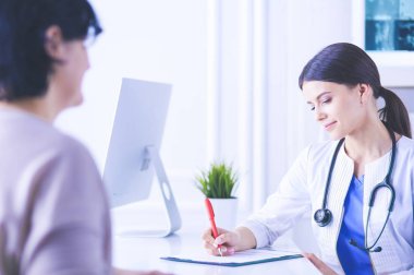 Doktor ve hasta hastane danışma odasında tıbbi sorunları tartışıyorlar. Doktor hasta formunu dolduruyor.