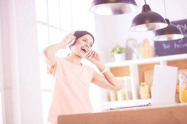 Mutfakta dururken kulaklıkla müzik dinleyen ve dizüstü bilgisayar kullanan neşeli bir genç kadının portresi