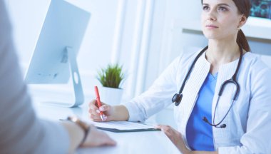 Doktor ve hasta hastane danışma odasında tıbbi sorunları tartışıyorlar. Doktor hasta formunu dolduruyor.