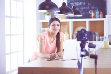 Mutfakta dizüstü bilgisayara benzeyen tariflerle gülümseyen genç bir kadın. Gıda blogcusu kavramı