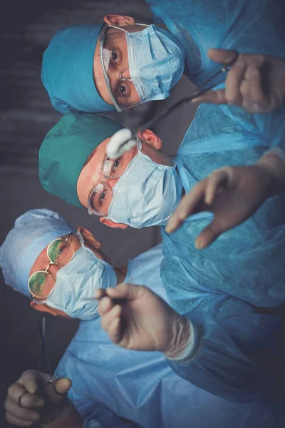 Grupo de cirujanos trabajando en quirófano tonificado en azul. Equipo médico realizando la operación —  Fotos de Stock