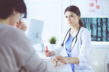 Kadın doktor hastane danışma odasında bir hastayı sakinleştiriyor, elini tutuyor.