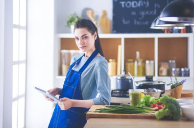 Mutfakta yemek yapmak için tablet bilgisayar kullanan genç bir kadın.