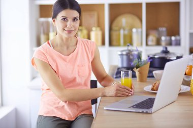 Mutfakta dizüstü bilgisayara benzeyen tariflerle gülümseyen genç bir kadın. Gıda blogcusu kavramı