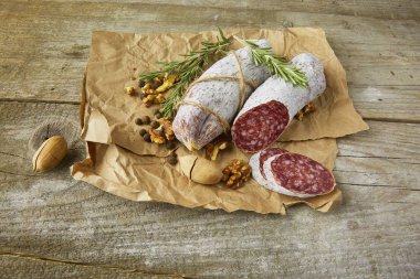 Italian salami wih sea salt, rosemary, garlic and nuts on paper. Rustic style. Top view. clipart