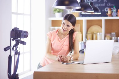 Mutfakta dizüstü bilgisayara benzeyen tariflerle gülümseyen genç bir kadın. Gıda blogcusu kavramı