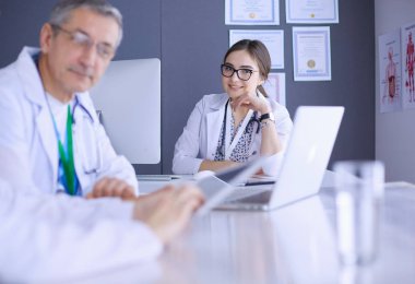 Ciddi bir tıbbi ekip parlak bir ofiste dizüstü bilgisayar kullanıyor.