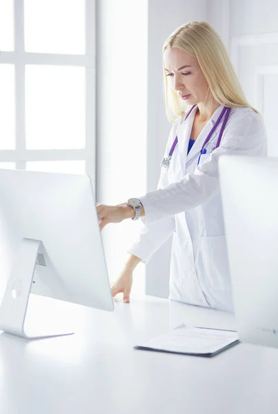 Fiatal nő orvos a munkahelyen, miközben a számítógép felé mutat a kórházi irodában.. — Stock Fotó