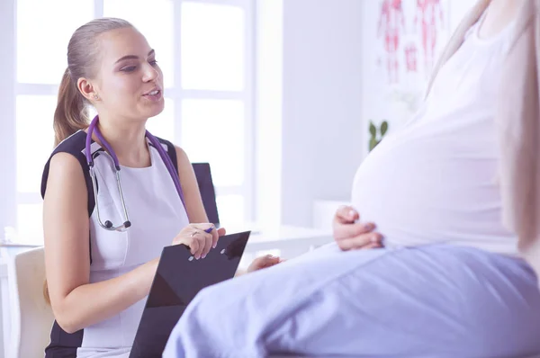 Jovem médica com estetoscópio e tablet falando com mulher grávida no hospital. — Fotografia de Stock