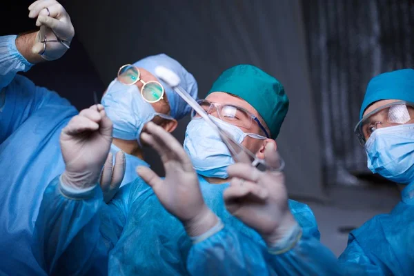 Grupo de cirurgiões no trabalho em sala de operações tonificada em azul. Equipe médica realizando operação — Fotografia de Stock