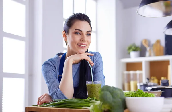 Mujer joven con vaso de sabroso batido saludable en la mesa en la cocina —  Fotos de Stock
