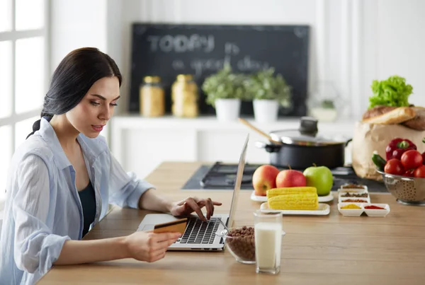 Smiling woman online shopping using computer and credit card in kitchen — Stock Photo, Image