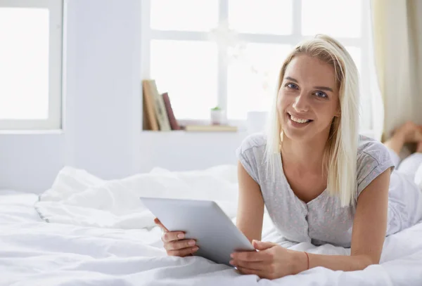 Chica sosteniendo tableta digital con pantalla en blanco y sonriendo a la cámara en el dormitorio — Foto de Stock