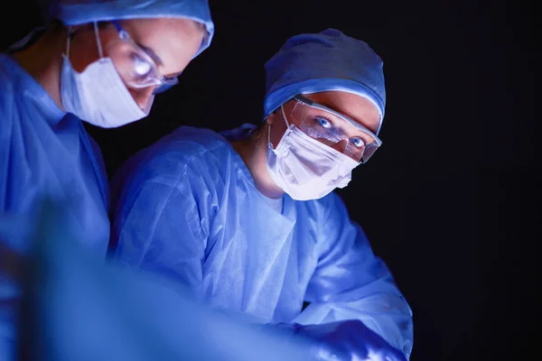 Equipe de médicos em cirurgia em um fundo escuro. — Fotografia de Stock