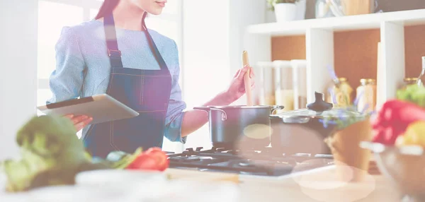 Ung kvinna använder en surfplatta dator för att laga mat i sitt kök — Stockfoto