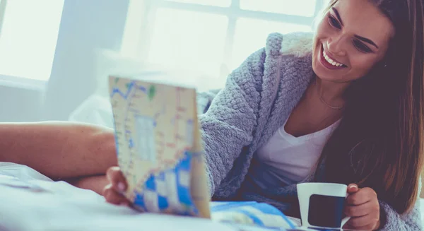 Relaxado jovem mulher sentada na cama com uma xícara de café e tablet digital — Fotografia de Stock