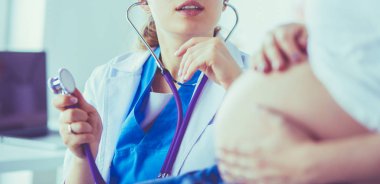 Genç bayan doktor klinikte hamile kadını muayene ediyor..