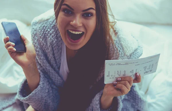 Avslappnad ung kvinna sitter på sängen med en kopp kaffe och digital tablett — Stockfoto