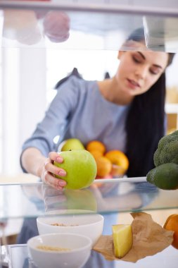 Gülümseyen kadın buzdolabından taze meyve alıyor, sağlıklı yiyecek konsepti.