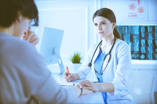 Vrouwelijke dokter kalmeert een patiënt in een ziekenhuis spreekkamer, houdt haar hand vast — Stockfoto