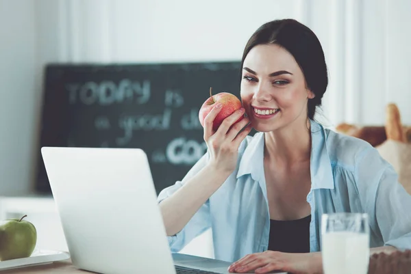Femme avec pomme et ordinateur portable assis dans la cuisine — Photo