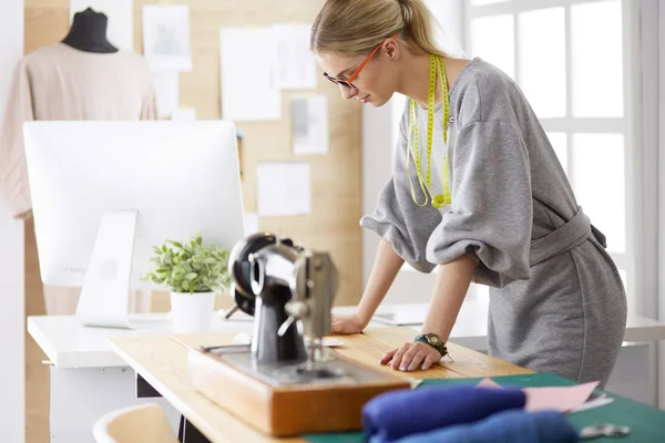 Het creëren van nieuwe modieuze stijlen. Vrolijke jonge vrouw naaien terwijl zitten op haar werkplek in mode workshop — Stockfoto