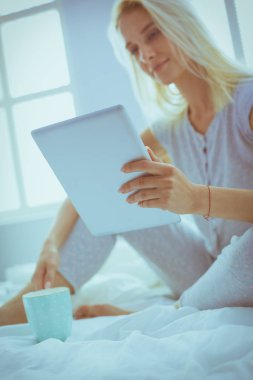 Elinde boş ekranlı dijital tablet tutan ve yatak odasında kameraya gülümseyen bir kız.