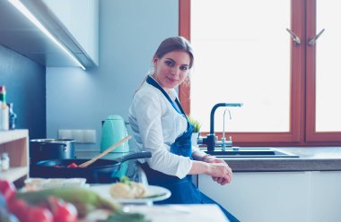 Mutfakta sobanın yanında duran genç bir kadın.