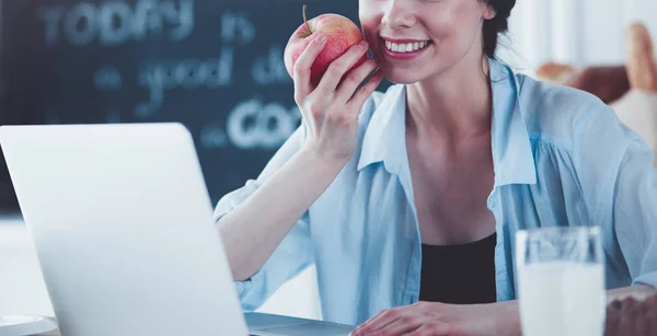 台所に座ってリンゴとラップトップを持つ女性 — ストック写真