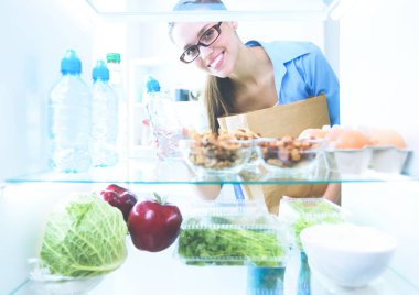 Sağlıklı yiyecek, sebze ve meyvelerle dolu açık buzdolabının yanında duran kadın portresi..
