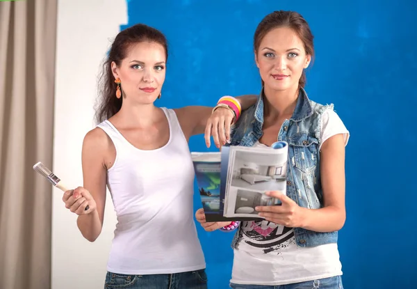 Dos hermosas mujeres jóvenes sosteniendo la paleta de colores, de pie cerca de la pared. Dos mujeres hermosas jóvenes —  Fotos de Stock