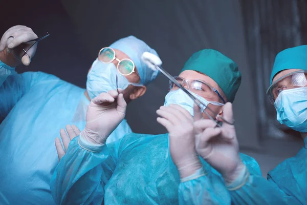 Grupo de cirurgiões no trabalho em sala de operações tonificada em azul. Equipe médica realizando operação — Fotografia de Stock