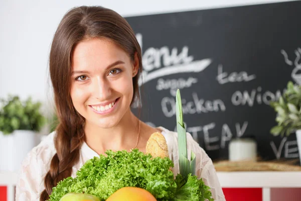 Leende ung kvinna med grönsaker stående i köket. Leende ung kvinna — Stockfoto