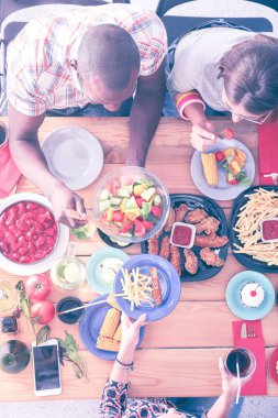 Ahşap masada otururken birlikte yemek yiyen bir grup insanın üst düzey görüntüsü. Masada yemek var. İnsanlar fast food yiyor..