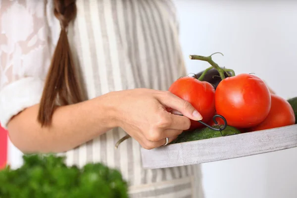 Smiling young woman holding vegetables standing in kitchen. Smiling young woman — Stock Photo, Image