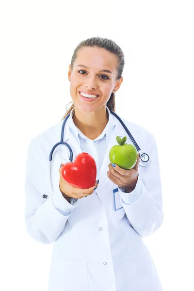 Красива усміхнена жінка-лікар тримає червоне серце і зелене яблуко. Жінка лікар — стокове фото