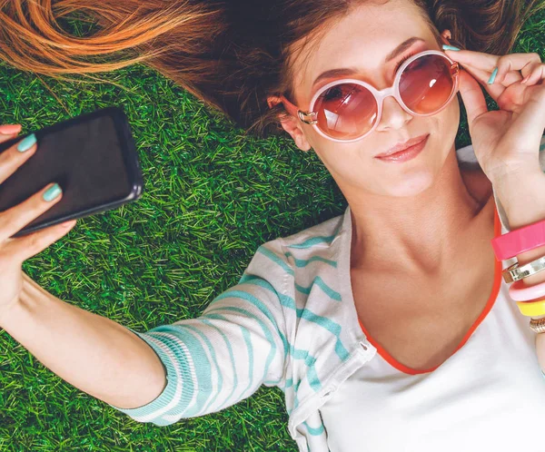 Mulher bonita fazendo selfie por seu telefone enquanto estava deitado na grama verde. Mulher bonita fazendo selfie — Fotografia de Stock