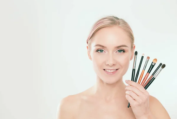 Portrait of beautiful young girl on white background with a perfect face with many hands holding makeup brush. — Stock Photo, Image