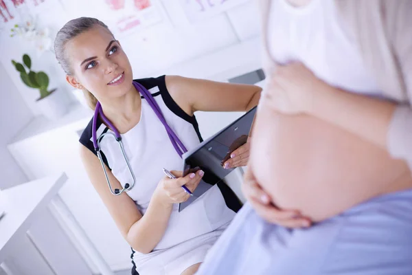 Young woman doctor with stethoscope and tablet speaking with pregnant woman at hospital. — Stock Photo, Image
