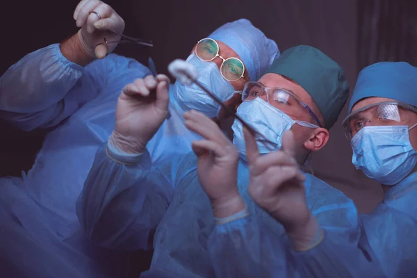 Grupo de cirurgiões no trabalho em sala de operações tonificada em azul. Equipe médica realizando operação — Fotografia de Stock