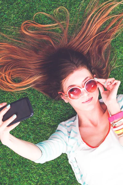 Mooie jonge vrouw die selfie maakt door haar telefoon terwijl ze in groen gras ligt. mooie jonge vrouw maken selfie — Stockfoto