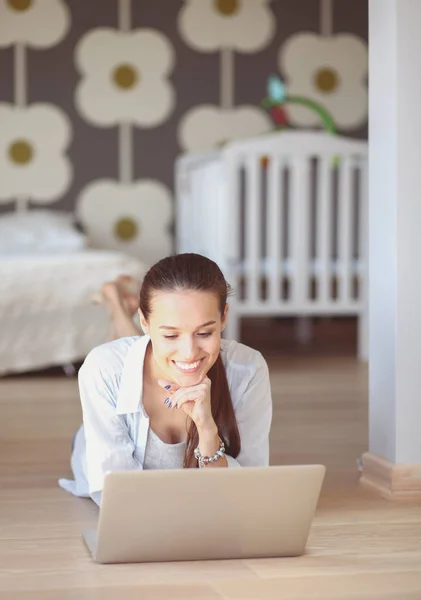 Jeune femme assise sur le sol près de lit d'enfant avec ordinateur portable. Jeune maman — Photo