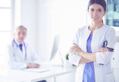 Hastanedeki danışma odasının arkasında kameraya gülümseyen bir doktor.