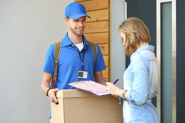 Repartidor sonriente con uniforme azul que entrega la caja de paquetes al destinatario: concepto de servicio de mensajería. Repartidor sonriente en uniforme azul — Foto de Stock