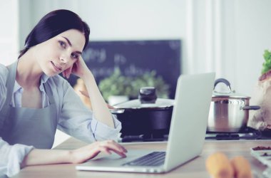 mutlu bir kadın mutfakta o onu laptop haber okuma