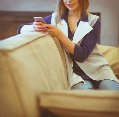 Genç bir kadın, beyaz odada rahat bir koltukta, elinde kahveyle oturuyor.