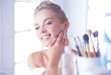 Bornozlu genç kadın banyo aynasına bakıyor.