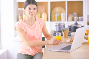 Mutfakta dizüstü bilgisayara benzeyen tariflerle gülümseyen genç bir kadın. Gıda blogcusu kavramı