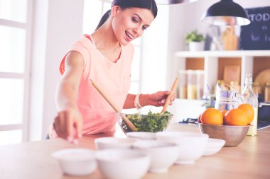 Gülümseyen genç kadın mutfakta taze salata karıştırıyor..