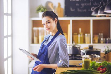Mutfakta yemek yapmak için tablet bilgisayar kullanan genç bir kadın.